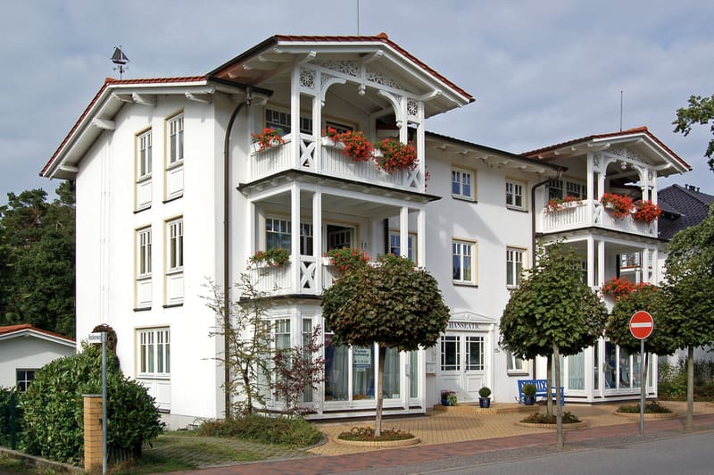 Weiß gestrichenes Haus in Bäderarchitektur an der Hauptstraße von Baabe, mit Holzveranden und Blumenkästen.