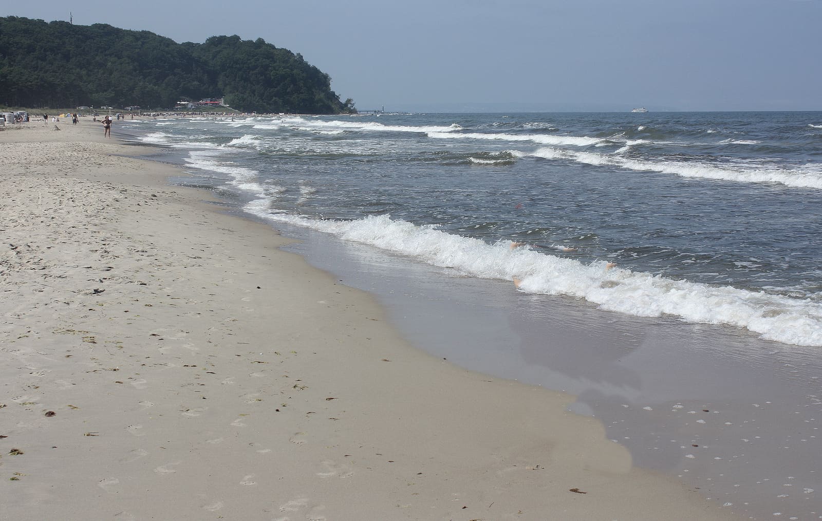Brandung am feinsandigen Ostseestrand von Baabe, im Hintergrund die bewaldete Küste.